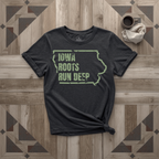 Iowa Roots Run Deep tee in black with sage print, laid flat on weathered wood