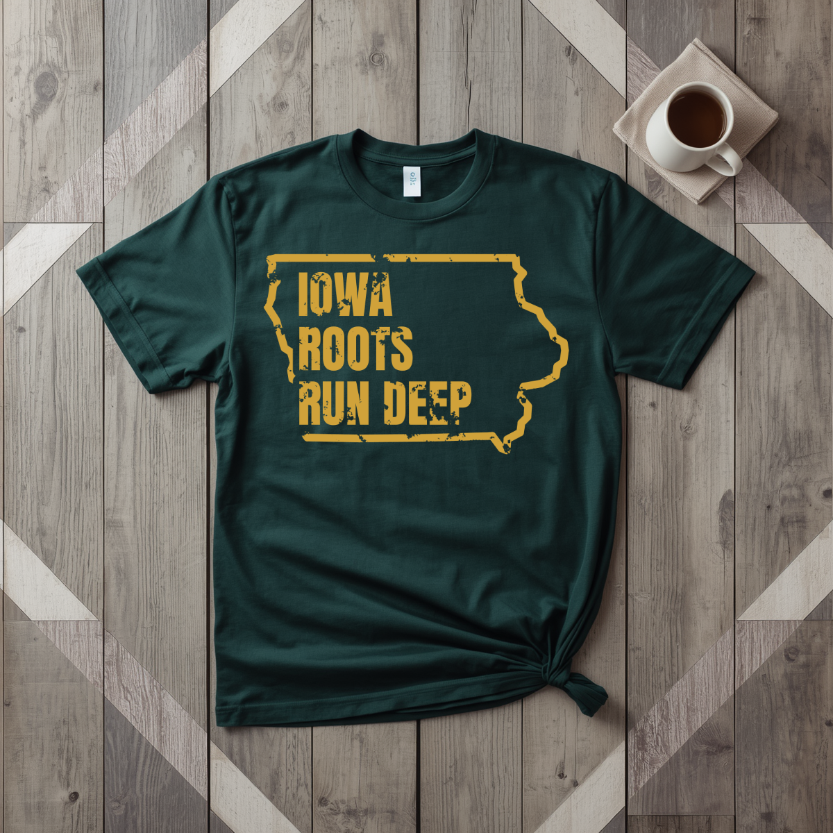 Iowa Roots Run Deep tee in forest green with mustard print, laid flat on weathered wood