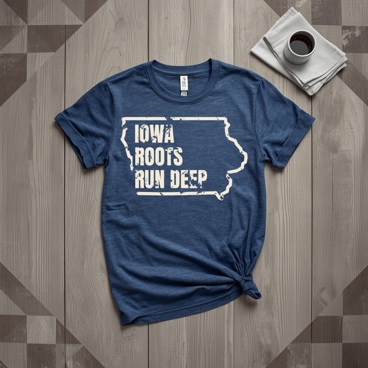 Iowa Roots Run Deep tee in heather navy with cream print, laid flat on weathered wood