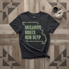 Missouri Roots Run Deep tee in black with sage print, laid flat on weathered wood
