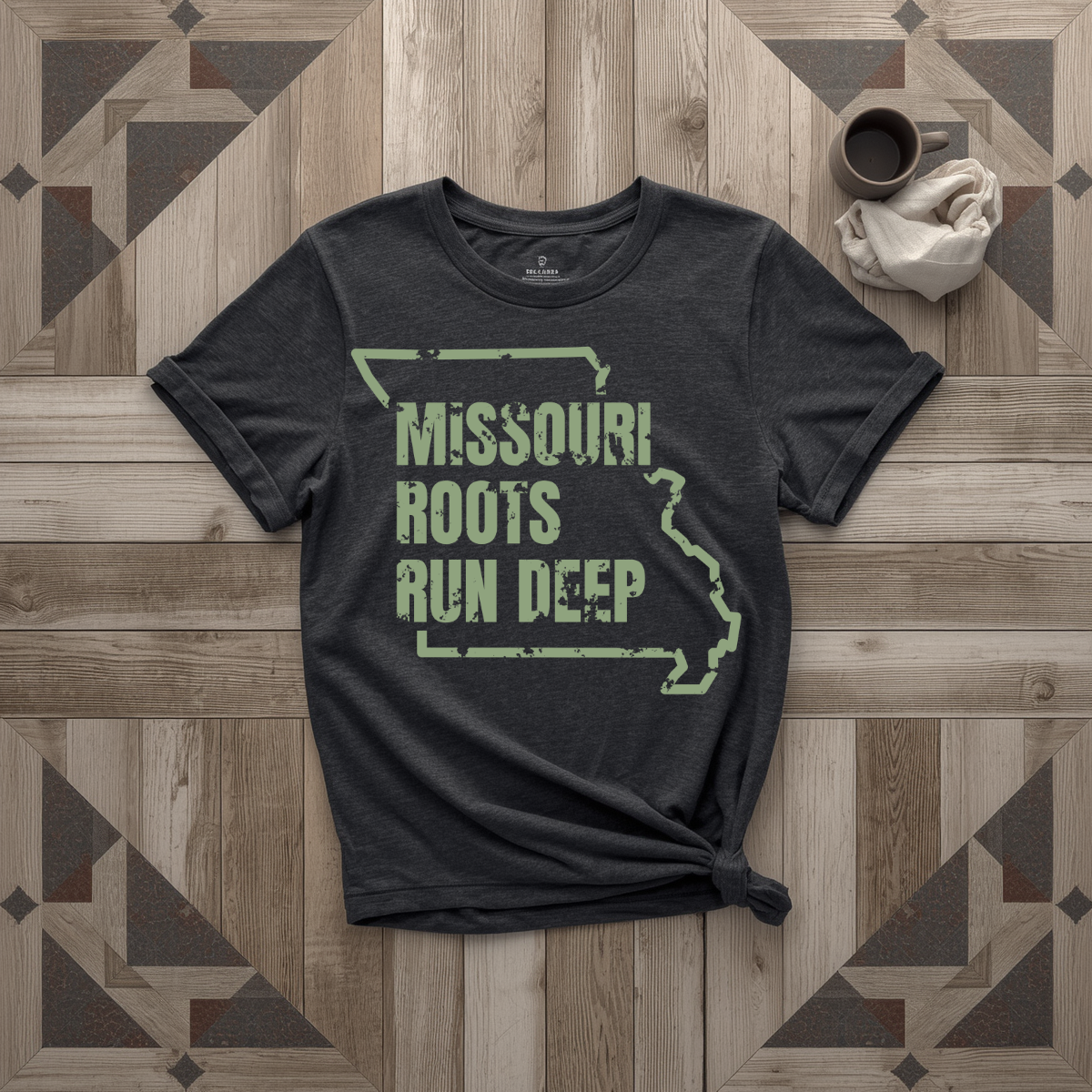 Missouri Roots Run Deep tee in black with sage print, laid flat on weathered wood