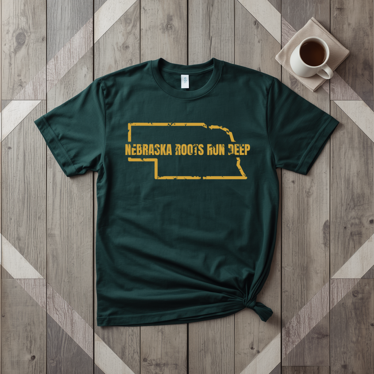 Nebraska Roots Run Deep tee in forest green with mustard print, laid flat on weathered wood