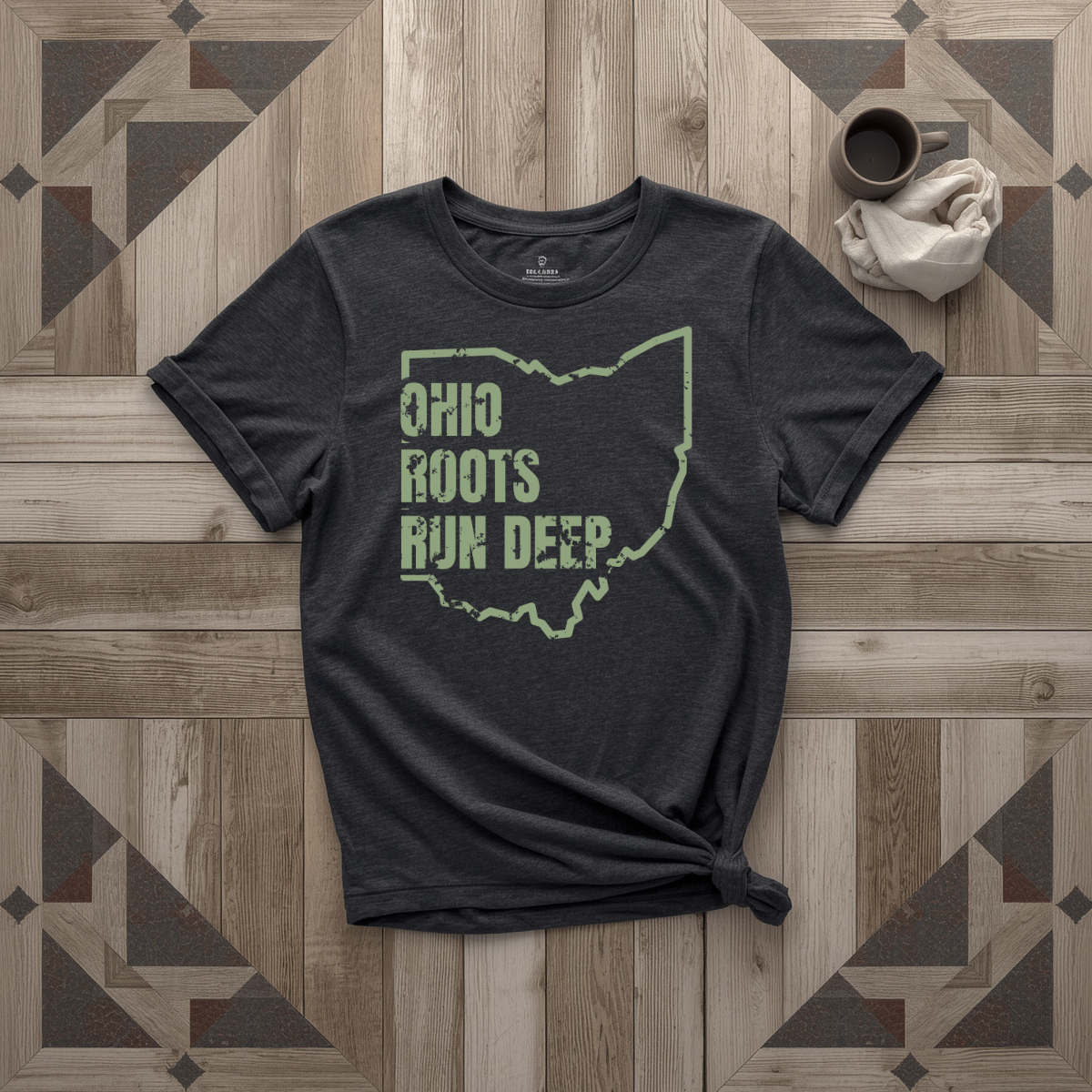 Ohio Roots Run Deep tee in black with sage print, laid flat on weathered wood