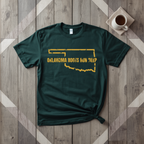 Oklahoma Roots Run Deep tee in forest green with mustard print, laid flat on weathered wood