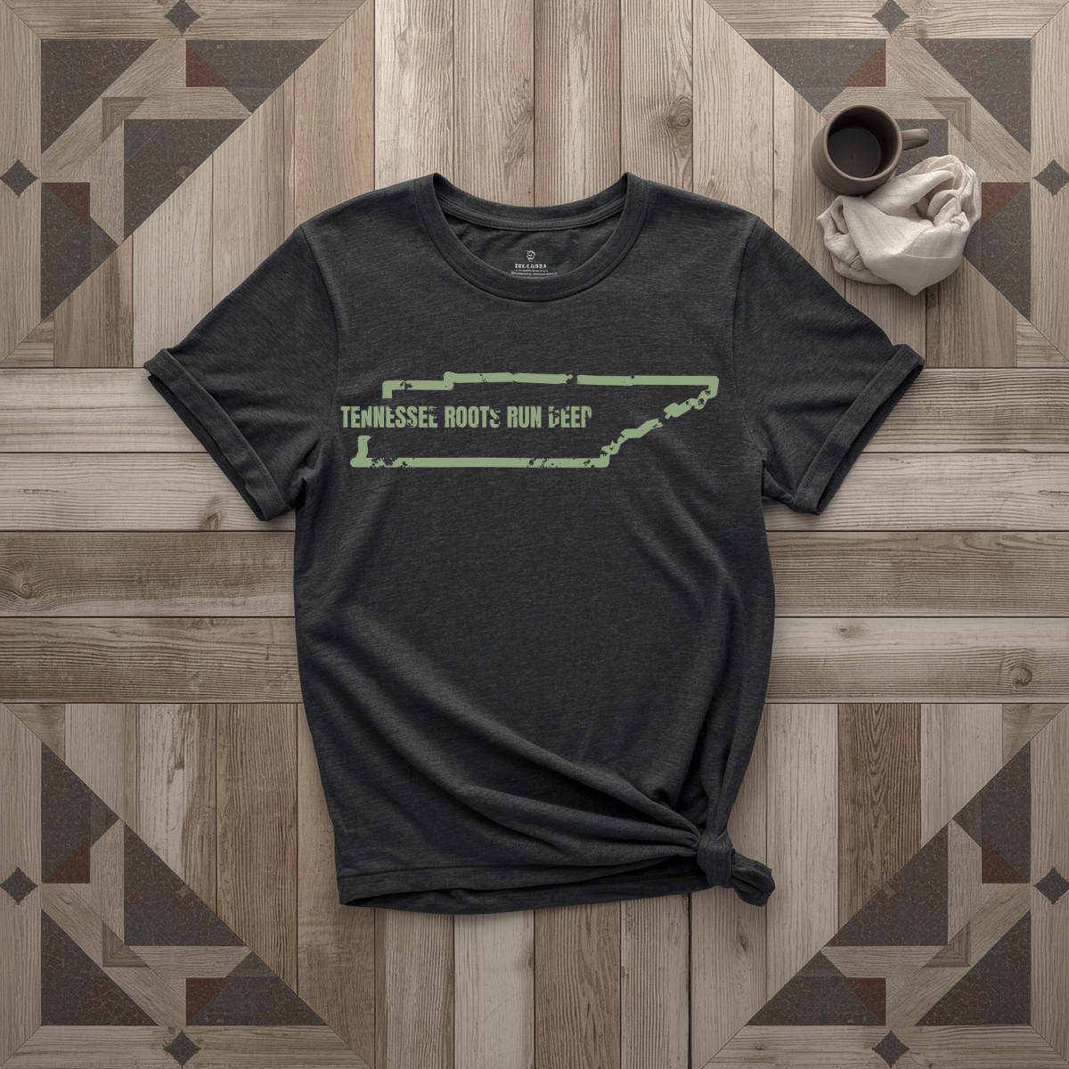 Tennessee Roots Run Deep tee in black with sage print, laid flat on weathered wood