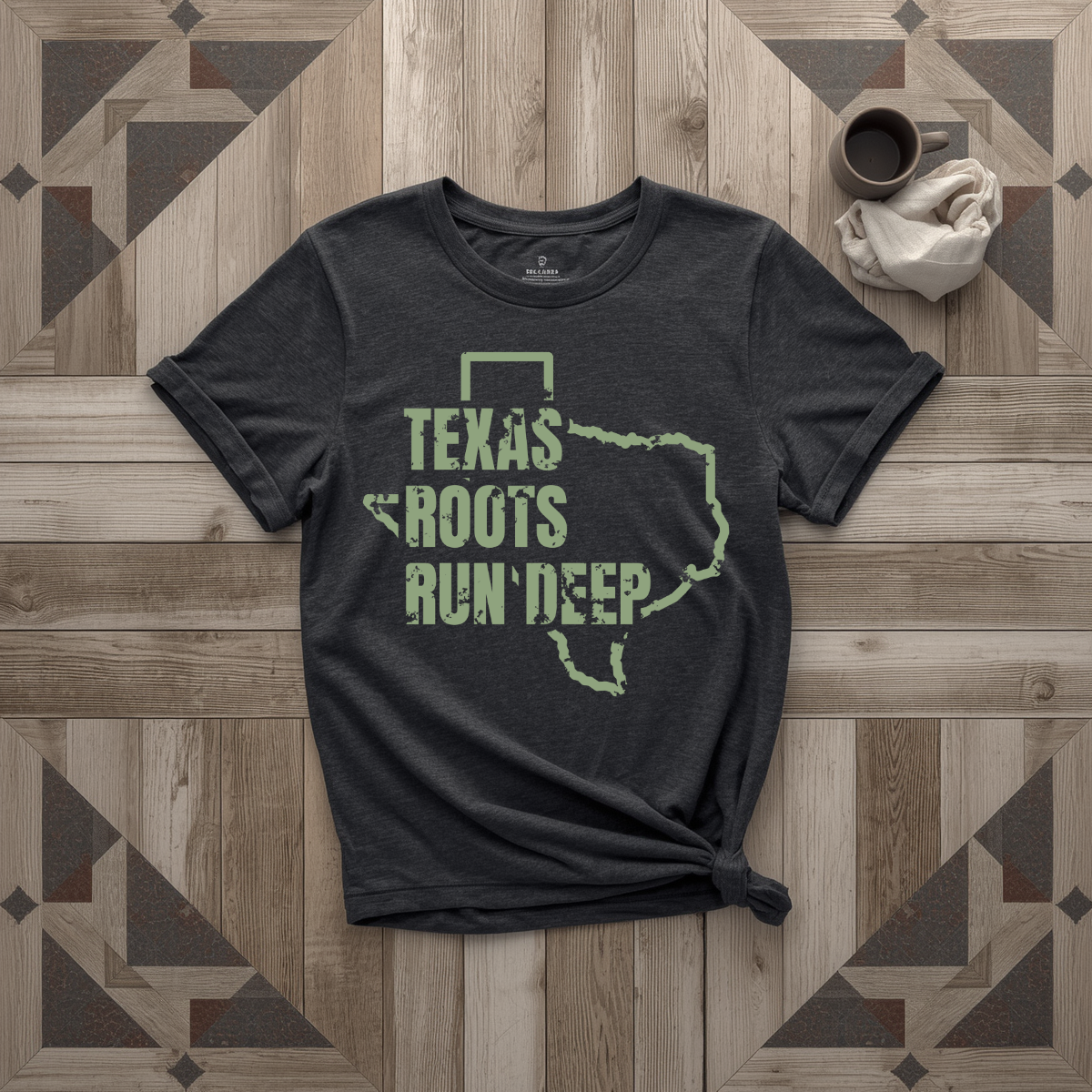 Texas Roots Run Deep tee in black with sage print, laid flat on weathered wood